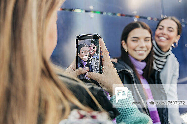 Young woman photographing friends through smart phone