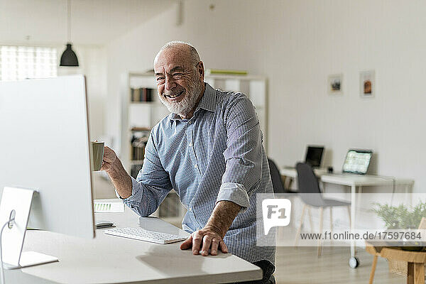 Happy businessman with computer sitting at desk