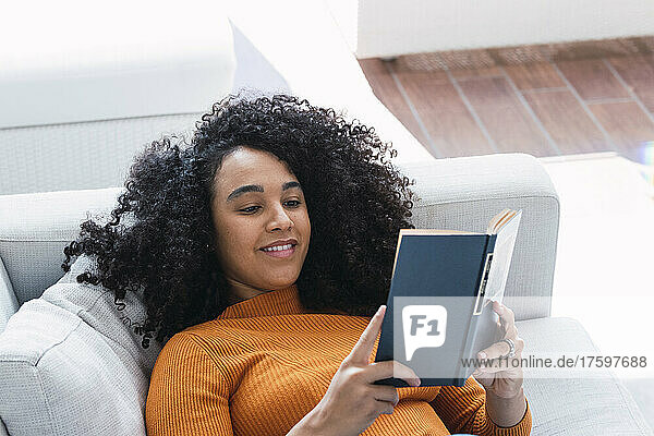 Woman reading book lying on sofa in living room