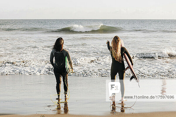 Surfers looking at sea holding surfboards at beach  Gran Canaria  Canary Islands