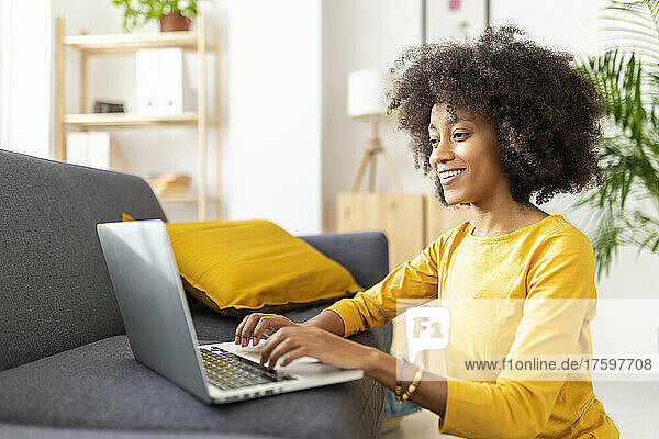 Happy young woman using laptop by sofa at home