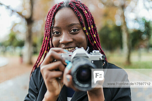 Young woman with red braided hair holding camera in park