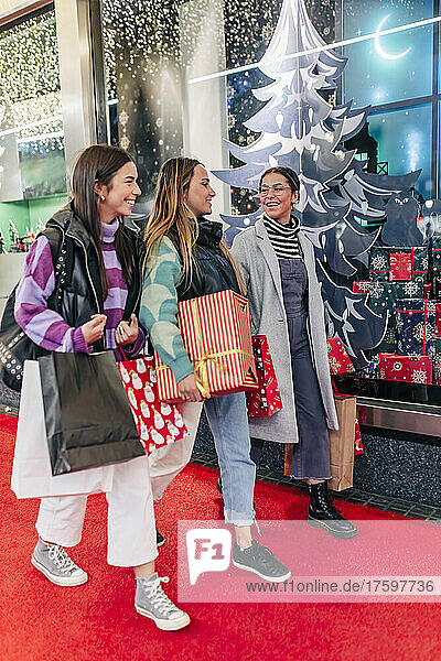 Smiling friends with shopping bags walking on footpath at Christmas