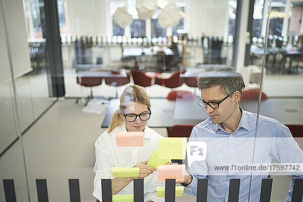 Businesswoman discussing with colleague over adhesive note in meeting room at office
