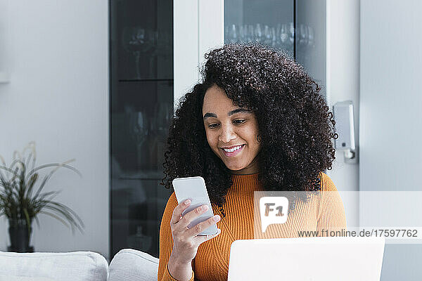 Woman with laptop using smart phone in living room