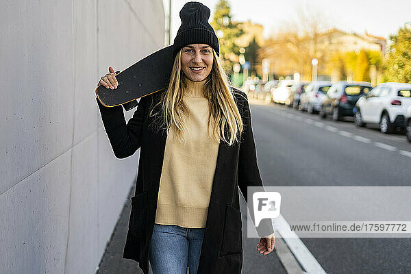 Smiling woman with skateboard walking on street