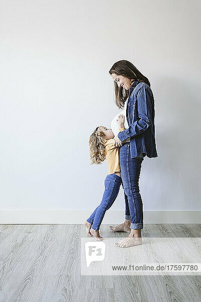 Pregnant mother with daughter standing by wall