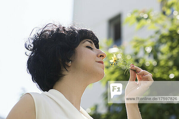 Woman with eyes closed smelling yellow flower on sunny day