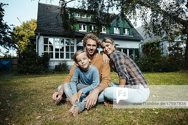 Smiling parents with son sitting outside house