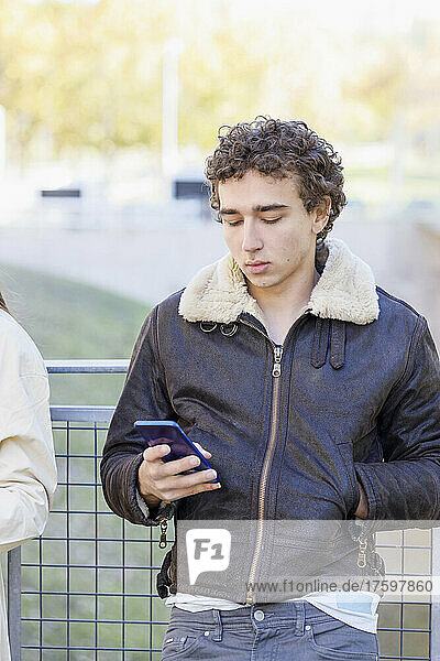Junger Mann benutzt Smartphone vor Geländer