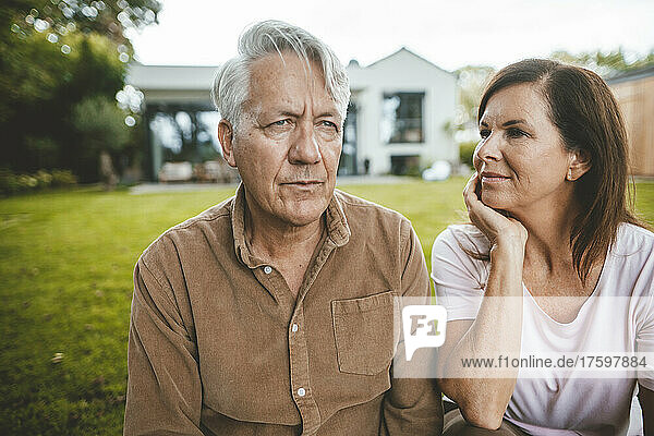 Woman with hand in head looking at man with white hair at backyard