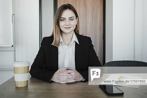 Young businesswoman with hands clasped sitting at desk in office