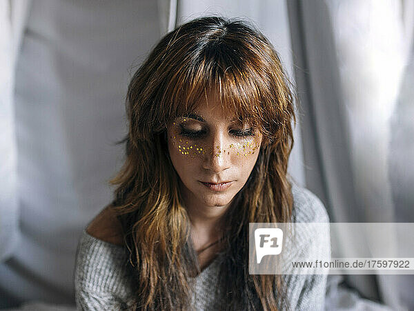 Young woman with glitter on face in front of backdrop
