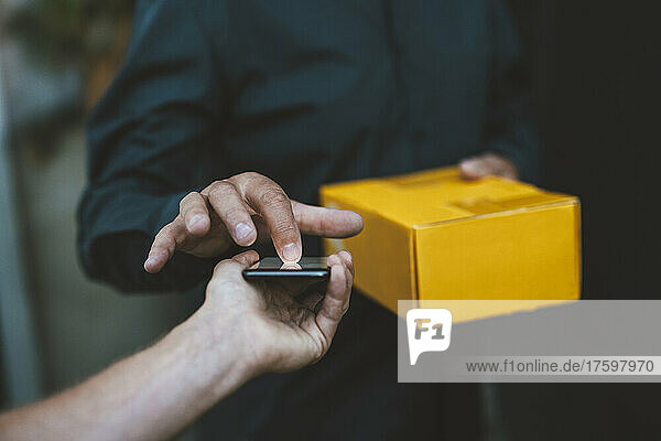 Senior man signing on mobile phone held by delivery person