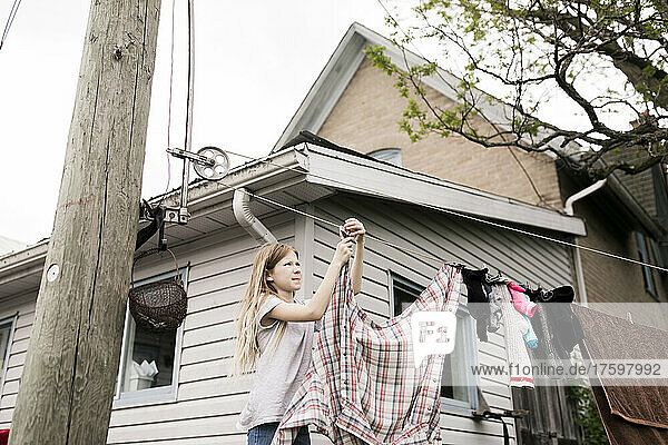 Mädchen hängt Kleidung an Seil vor Haus