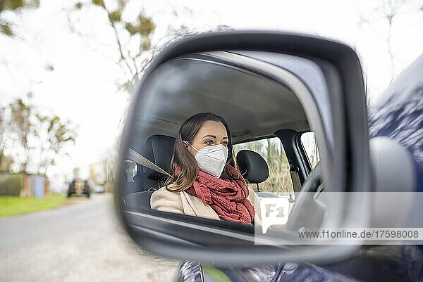 Reflection of woman wearing mask on car's side-view mirror