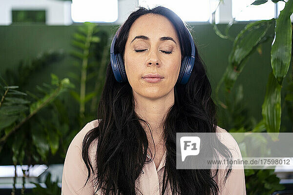 Businesswoman with eyes closed listening music through headphones in coworking office