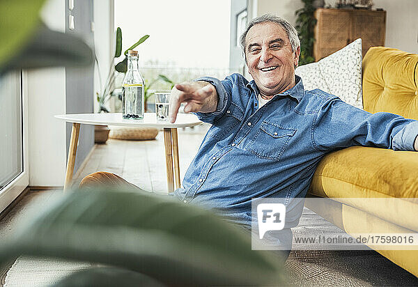 Happy senior man gesturing by sofa in living room at home