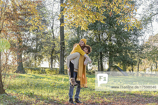 Young man giving piggyback ride to girlfriend at autumn park