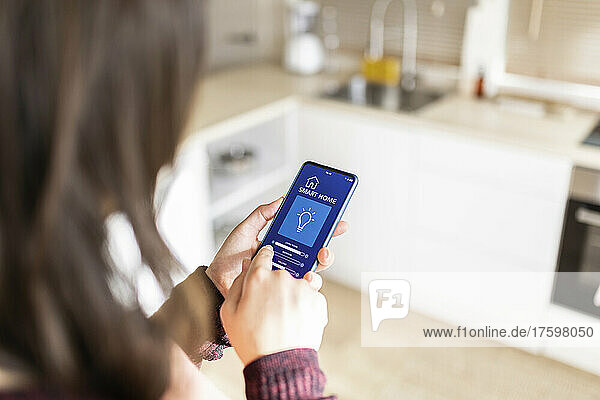 Frau passt die Helligkeit mithilfe einer Smart-Home-Anwendung auf dem Mobiltelefon zu Hause an