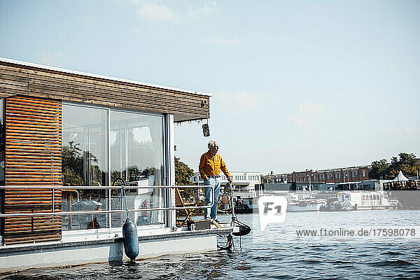 Senior man standing by railing at houseboat on sunny day