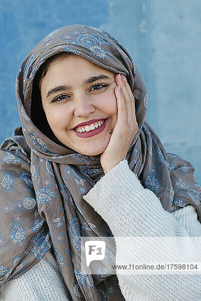 Lächelnde junge Frau mit Hijab vor der Wand