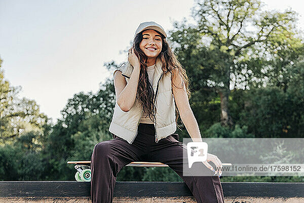 Smiling young woman sitting on skateboard in park