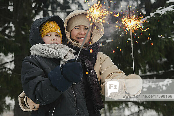 Smiling mother with son looking at sparklers in winter