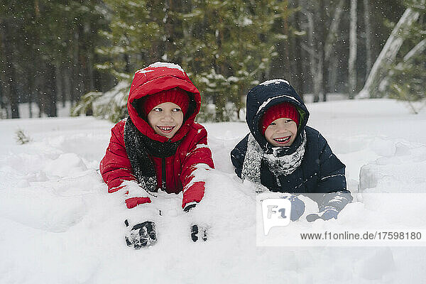 Playful twin brothers lying on snow in winter