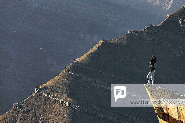 Female hiker admiring landscape of Caucasus Mountains from edge of cliff