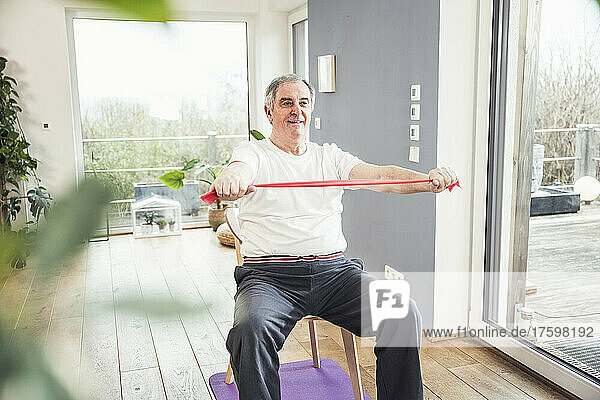 Senior man with resistance band sitting on chair working out at home