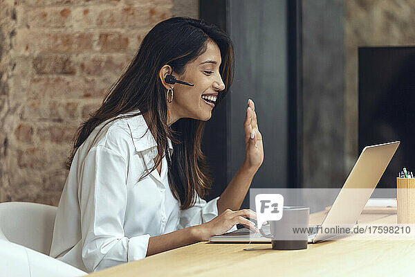 Happy businesswoman waving hand on video call in coworking office
