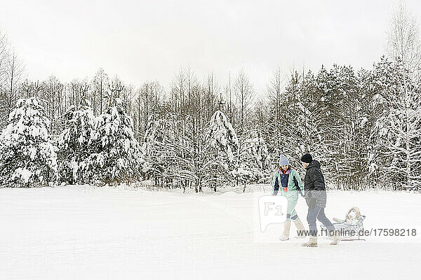 Eltern ziehen Tochter auf Schlitten und laufen im Winter auf Schnee