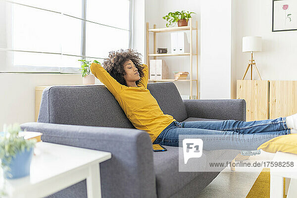 Young woman with hands behind head relaxing on sofa in living room
