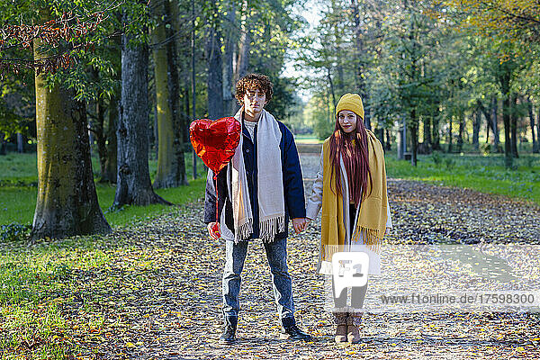 Couple holding hands standing with red heart shape balloon at park