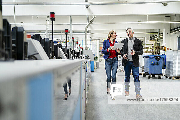 Businessman and businesswoman sharing ideas walking in production wall