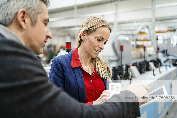 Businessman discussing over tablet PC with blond businesswoman in factory