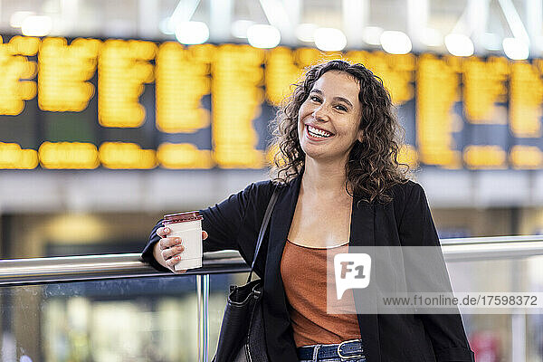 Happy young woman with disposable coffee cup at railroad station