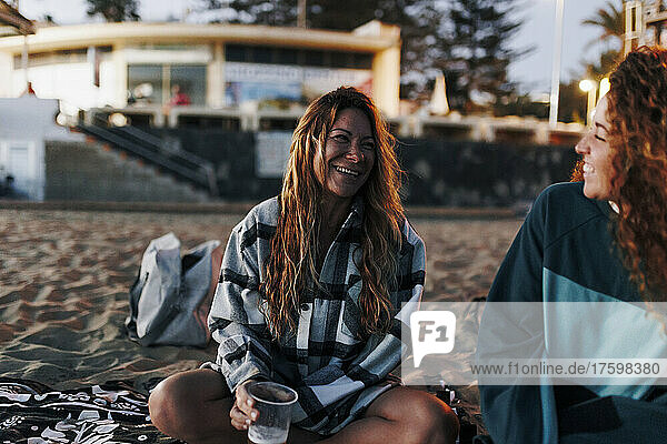 Fröhliche Frau hält einen Bierbecher in der Hand und unterhält sich mit einer Freundin am Strand