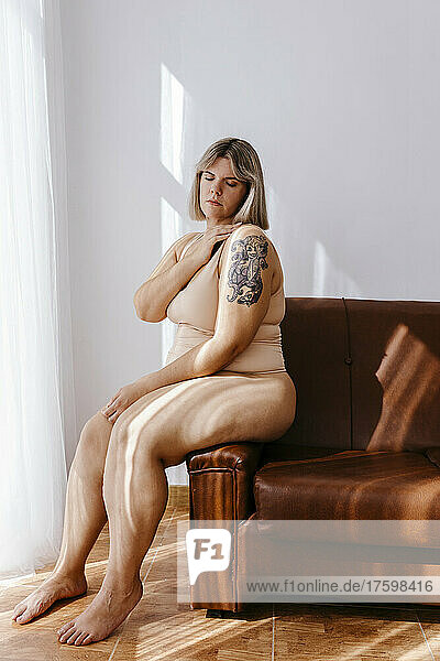 Curvy woman with eyes closed sitting on sofa