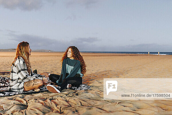 Frau unterhält sich mit einer Freundin  die am Strand im Sand sitzt