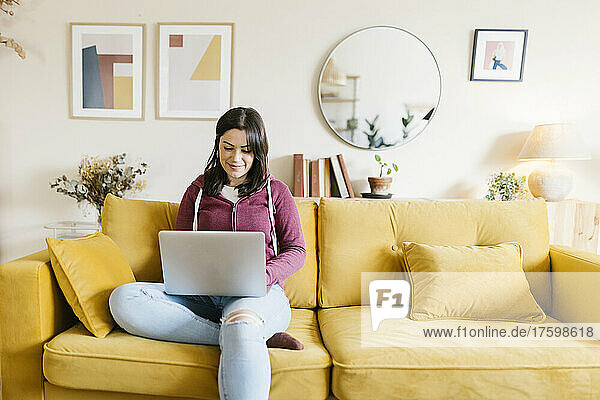 Junge Frau sitzt mit Laptop auf dem Sofa im Wohnzimmer