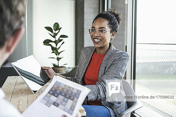Lächelnde Geschäftsfrau diskutiert über Tablet-PC mit Kollegen im Büro