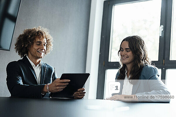 Smiling businessman using tablet PC discussing with colleague at desk in office