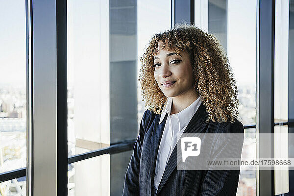 Young businesswoman with curly hair smiling near window in office