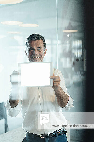 Smiling businessman showing blank screen of tablet PC at office