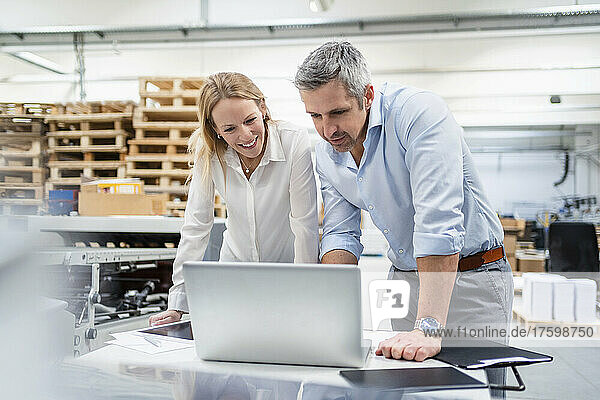 Businessman and businesswoman sharing laptop at desk in factory