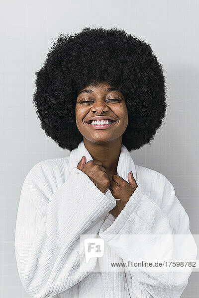 Happy young woman with bathrobe in front white wall
