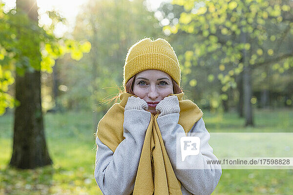 Smiling woman wearing yellow knit hat and scarf in autumn park