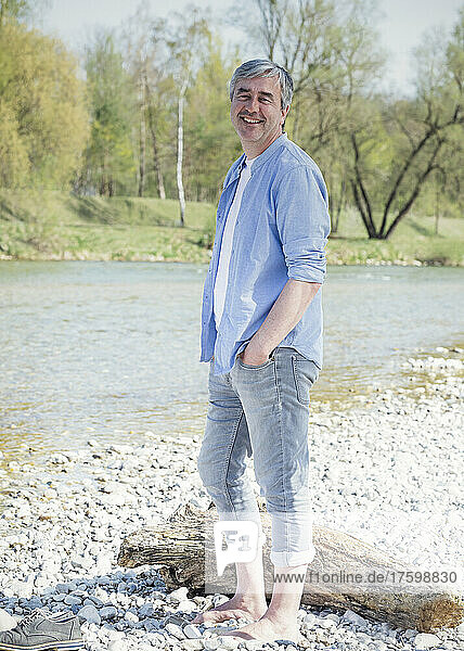 Happy man with hand in pocket standing by river